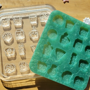 May include: Two silicone molds for making resin crafts. One mold is clear and the other is green. Both molds have various shapes of food and drinks, such as coffee cups, pretzels, and french fries.