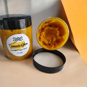 May include: Two jars of turmeric sugar scrub, one open and one closed. The jar is labeled "SRC Turmeric Glow Emulsified Sugar Scrub 10 oz (283g)".