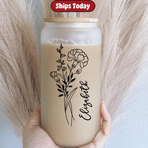 Op de afbeelding: Een herbruikbare waterfles van helder glas met een bamboe deksel. De fles heeft een zwart-witte lijntekening van bloemen en de naam "Elizabeth" erop.