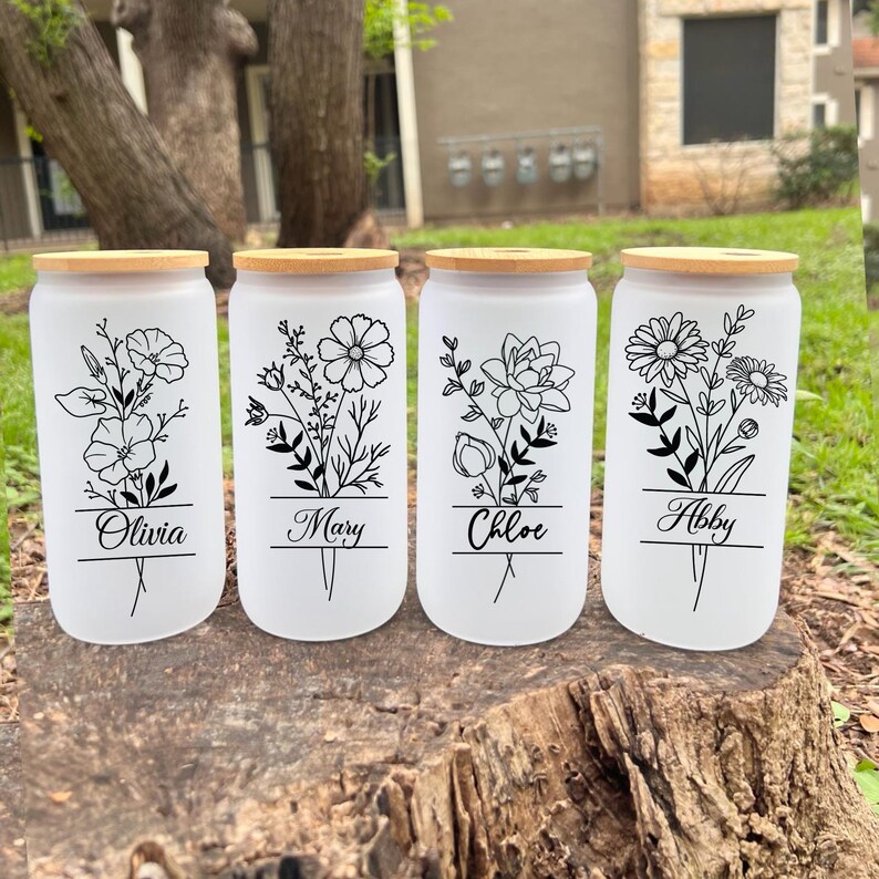 May include: Four white frosted glass canisters with bamboo lids and black floral designs. Each canister has a name printed on the front: Olivia, Mary, Chloe, and Abby.