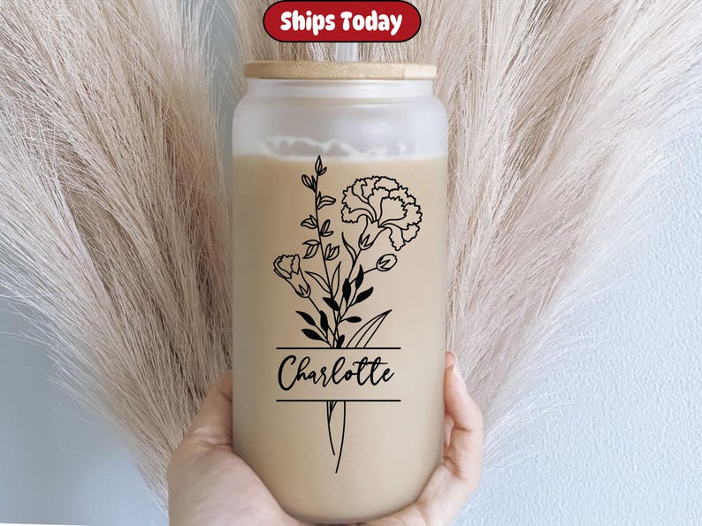 May include: A clear glass tumbler with a bamboo lid and a black floral design. The design includes a bouquet of flowers with the name "Charlotte" written in a black banner.
