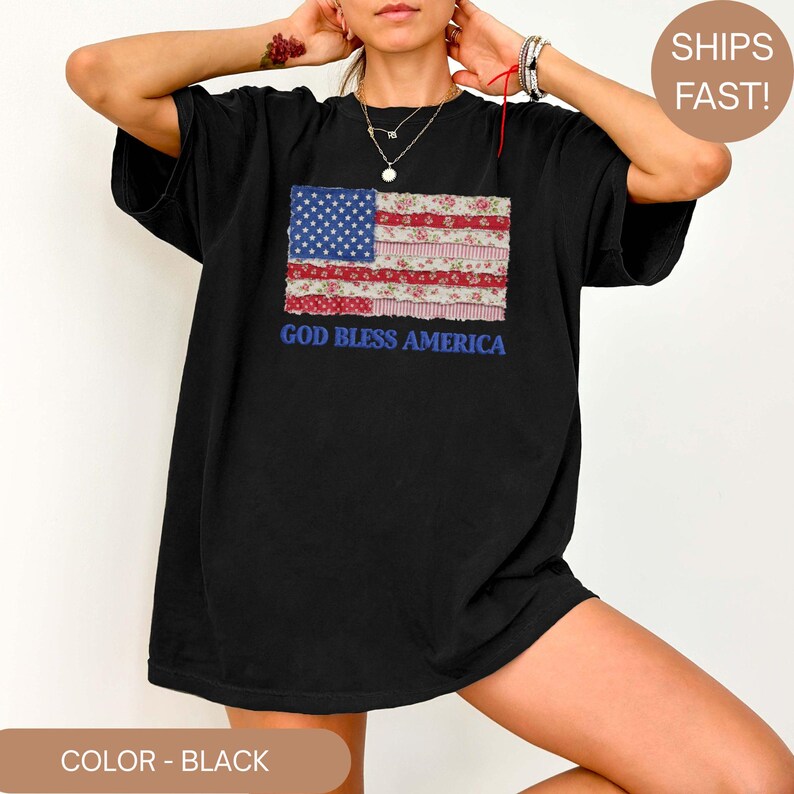 Puede incluir: Camiseta negra con un dise&ntilde;o de bandera americana de retazos. La bandera incorpora un campo azul de estrellas, rayas rojas y blancas y patrones florales. La frase "GOD BLESS AMERICA" est&aacute; impresa en azul debajo.