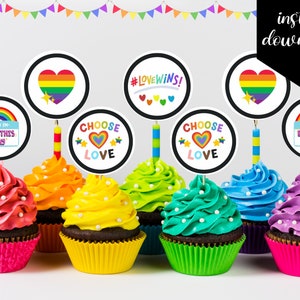 Może przedstawiać: Sześć ozdób do babeczek w tęczowych kolorach z różnymi napisami, w tym "Hello I'm Born This Way", "Choose Love" i "#LoveWins!".