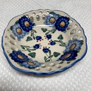 May include: A white ceramic plate with a blue and brown floral design. The plate has a scalloped edge and a cut-out design around the rim.