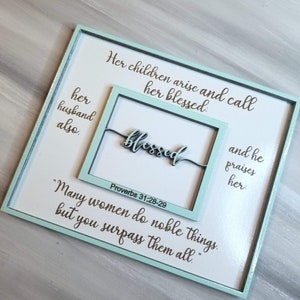May include: A light blue wooden sign with a white background and the text "Her children arise and call her blessed: her husband also. blessed Proverbs 31:28-29 "Many women do noble things, but you surpass them all."