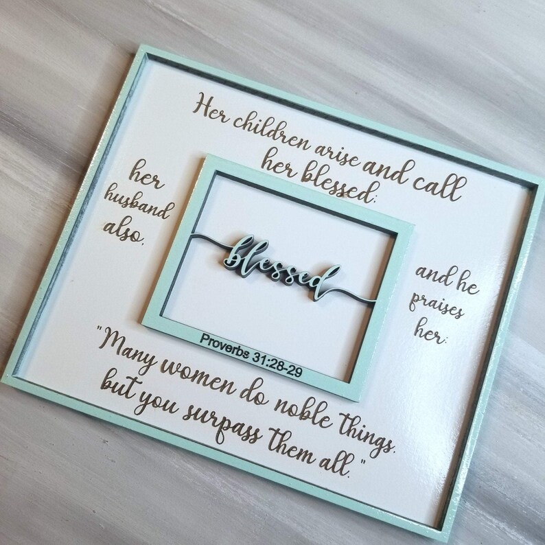 May include: A light blue wooden sign with a white background and the text "Her children arise and call her blessed: her husband also. blessed Proverbs 31:28-29 "Many women do noble things, but you surpass them all."