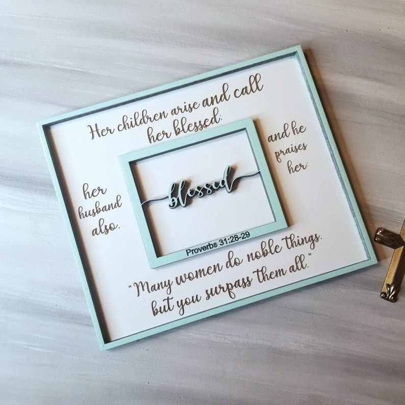 May include: A light blue wooden sign with a white background and the text "Her children arise and call her blessed. Her husband also. Blessed. Proverbs 31:28-29 "Many women do noble things, but you surpass them all."