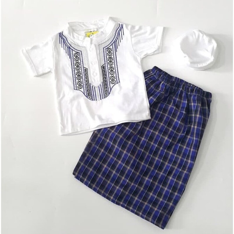 May include: A white short-sleeved shirt with a blue and white embroidered design, a blue and white plaid skirt, and a white cap. The shirt has a button closure at the neck.