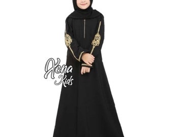 May include: A black abaya with gold embroidery on the sleeves. The abaya has a zipper closure and a long, flowing skirt. The model is wearing a black headscarf.