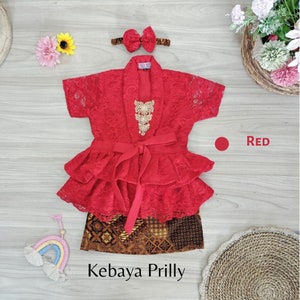 May include: Red lace kebaya with a ruffled skirt and a gold decorative piece. The kebaya is paired with a brown and gold patterned skirt. The text "Kebaya Prilly" is visible below the skirt. The color "Red" is indicated with a red circle.