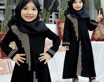 May include: Two young girls wearing black abayas with gold embroidery. The abayas have long sleeves and are floor-length. The girls are wearing headscarves and have their hair covered.