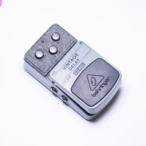 May include: A silver Behringer VD400 Vintage Delay guitar pedal with a gray fabric top and three knobs. The pedal has a black foot switch and the text "Vintage Delay VD400" is printed on the front.