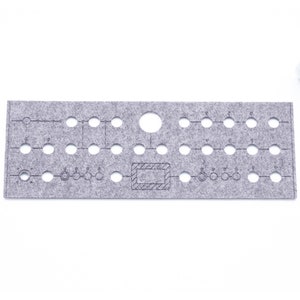 May include: A gray felt board with a grid of holes and a printed design. The design includes circles, lines, and a rectangle with a hatched pattern. The board is used for organizing and displaying items.