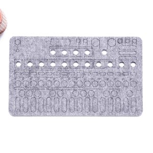 以下が含まれることがあります： 電子機器用と思われる、様々な切り抜き形状と穴のある灰色のフェルトパネル。小さな鉢植えの多肉植物が左上にあります。「WaveTable 2025」の著作権表示が右下にあります。