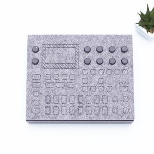 May include: A grey felt pad with a black screen and buttons. The pad has a grid of squares and circles, resembling a musical keyboard.