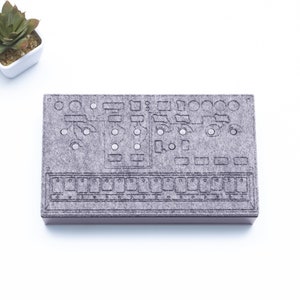 May include: A gray felt board with a design of a synthesizer with knobs and buttons. The board is a DIY project for music lovers.