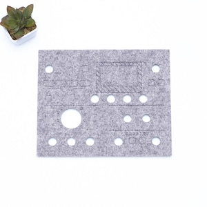 Peut inclure: Un tapis en feutre gris avec des découpes pour des boutons, des boutons et un écran. Le tapis est conçu pour être utilisé avec un synthétiseur ou d'autres équipements de musique électronique.