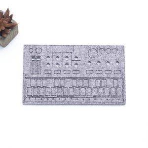 Könnte beinhalten: Eine graue Filz-Tastaturmatte mit einem Design eines Synthesizers. Die Matte ist rechteckig und aus einem weichen, strukturierten Material gefertigt.
