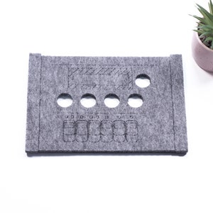 May include: A grey felt organiser with cutouts for small items. The organiser has a rectangular shape with rounded corners and a small rectangular cutout in the top centre.