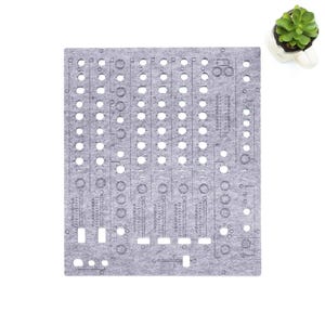 Könnte beinhalten: Eine graue Modularsynthesizer-Platte aus Filz mit zahlreichen kreisförmigen und rechteckigen Aussparungen. Die Platte hat aufgedruckte Markierungen und ist für die elektronische Musikproduktion konzipiert. Eine kleine Sukkulentenpflanze in einem weißen Topf befindet sich in der oberen rechten Ecke.