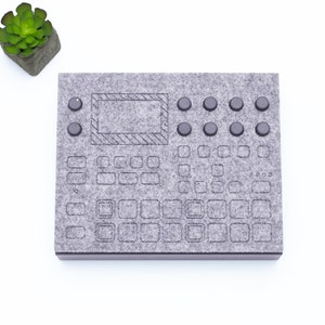 Könnte beinhalten: Ein graues Filzpad mit einer schwarzen Umrandung eines Musiksamplers. Das Pad hat 16 Tasten und 8 Knöpfe.