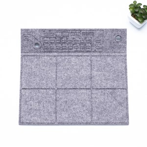 May include: A gray felt drum pad with a grid of four squares and a keyboard design at the top. The pad has two holes on the top right and left corners.