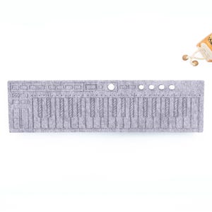May include: A gray felt keyboard with a full set of keys and control buttons. The keyboard is rectangular and lies flat on a white surface. A small decorative plant in a pot is in the upper right corner.