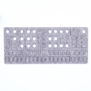 Peut inclure: Un panneau en feutre gris avec des cercles et des formes rectangulaires découpés, ressemblant à un panneau de commande de synthétiseur. Le panneau présente un design détaillé avec diverses ouvertures et lignes gravées. Une petite plante succulente dans un pot carré blanc est dans le coin supérieur gauche.