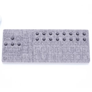 May include: A gray felt electronic music controller with multiple buttons and square pads. The controller has a rectangular shape and is placed on a white surface. A small succulent plant in a white pot is in the upper left corner.