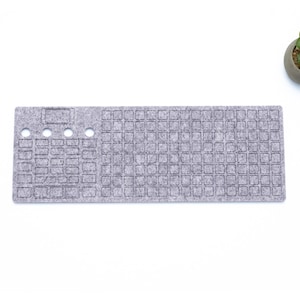 May include: A gray felt keyboard mat with a grid pattern and four small holes. The mat is designed to protect a keyboard from spills and dirt.