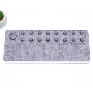 May include: A gray felt MIDI controller with a round knob and 16 square buttons. The controller has a white border.