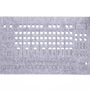 May include: A gray felt panel with cut-out holes and etched lines, resembling a control panel. The design includes various button and slider shapes. A small potted plant is in the upper right corner. The text "WaveTable 2025" is in the lower right corner.