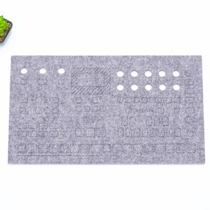Peut inclure: Un tapis de clavier en feutre gris avec des découpes pour les touches et un écran. Le tapis a une surface texturée et est conçu pour protéger un clavier des éclaboussures et de la saleté.