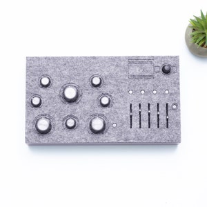 May include: A gray felt soundboard with multiple knobs and sliders. The soundboard has a circular button in the top right corner.