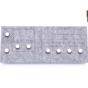 Peut inclure: Un tableau en feutre gris avec un motif imprimé et des boutons blancs. Le tableau est utilisé pour organiser et planifier des tâches.