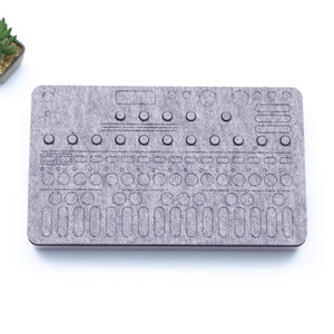 May include: A gray felt pad with a design of a synthesizer control panel. The design includes knobs, buttons, and sliders.
