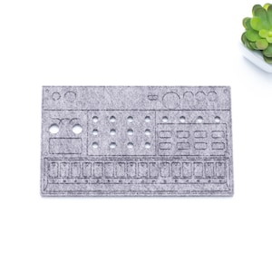 Könnte beinhalten: Ein grauer Filzuntersetzer mit einem Design eines Synthesizers. Der Untersetzer hat eine strukturierte Oberfläche und ist rechteckig.