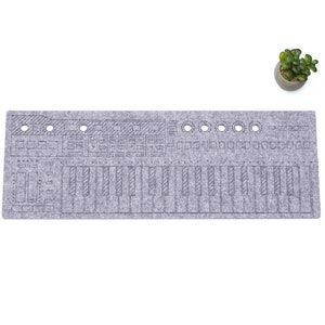 Puede incluir: Una alfombrilla de teclado de fieltro gris con un diseño de teclado de sintetizador. La alfombrilla tiene agujeros para cables y está diseñada para proteger las superficies de los arañazos.