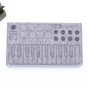 Può includere: Una tastiera in feltro grigio con un contorno nero. La tastiera ha 16 pad, 8 manopole e 25 tasti.