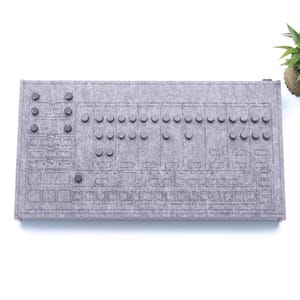 Peut inclure: Un clavier en feutre gris avec des boutons noirs. Le clavier a une grille et est conçu pour ressembler à un synthétiseur vintage.