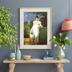 May include: A framed painting of a woman in a white dress standing in a garden setting. She is holding a bouquet of flowers and is looking to the left. The painting is set against a blue wall.