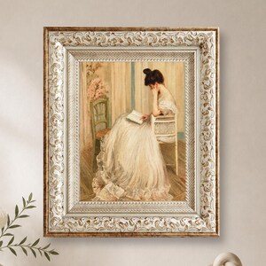 May include: A framed oil painting depicting a person with dark hair styled in an updo, wearing a long, flowing cream-colored gown, seated on a wooden chair while reading an open book. The frame is ornate, featuring a gold and white finish.