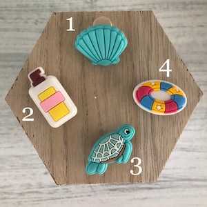 May include: A wooden hexagonal display board with four colorful charms: a blue seashell, a yellow and pink bottle of sunscreen, a blue turtle, and a red, yellow, and blue life preserver.