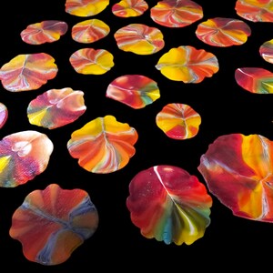 May include: A collection of colorful, abstract leaf-shaped art pieces. Each piece features a unique blend of red, yellow, and orange hues, with some including hints of blue and green. The pieces are arranged against a black background.