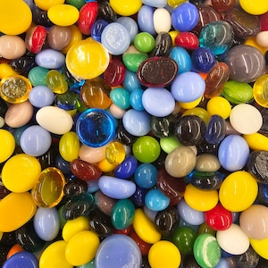 May include: A large collection of colorful glass pebbles in various shapes and sizes. The pebbles are mostly round and oval, with some being more irregular. The colors include yellow, blue, green, red, brown, and white.