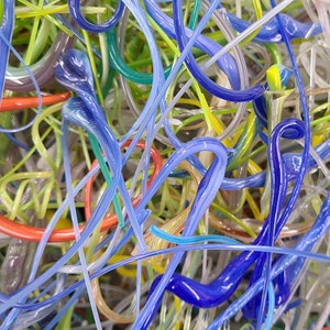 May include: A close-up of a tangled mass of colorful glass rods. The rods are in various shades of blue, green, yellow, and orange. The glass rods are arranged in a random pattern, creating a visually interesting and abstract design.
