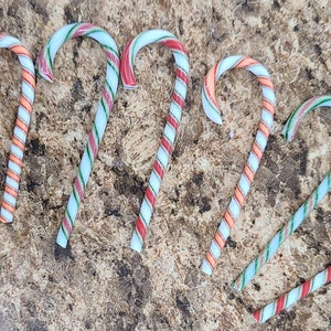 May include: Six candy canes with red, white, and green stripes. The candy canes are arranged in a semi-circle on a brown surface.