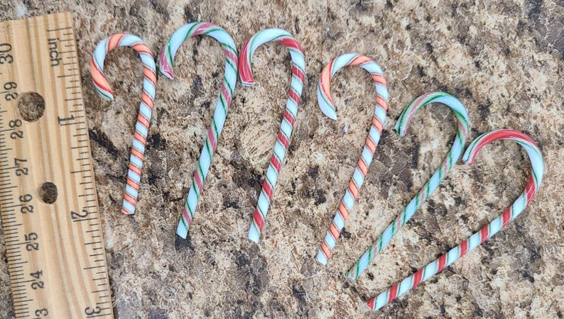 May include: Six candy canes with red, white, and green stripes. The candy canes are arranged in a semi-circle on a brown surface.