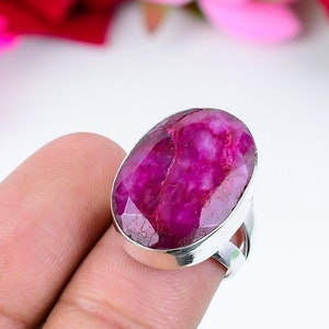 Puede incluir: Un anillo de plata con una gran piedra preciosa ovalada de color rosa. La piedra preciosa tiene un corte facetado y un color rosa intenso.