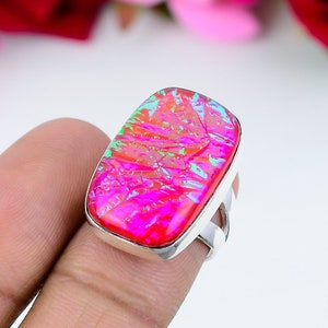May include: A rectangular silver ring featuring a vibrant, multi-colored gemstone. The stone displays shades of pink, red, and green, with a cracked, textured appearance. The ring has a simple, modern design, perfect for everyday wear.